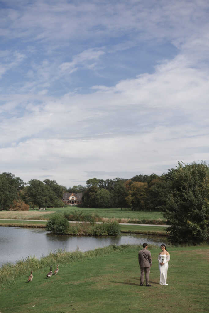 Brautpaar auf einer Wiese am See vor einem Herrenhaus unter weitem Himmel